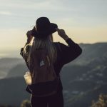 Solo Travel - woman in gray hoodie and black pants wearing black hat standing on top of mountain during