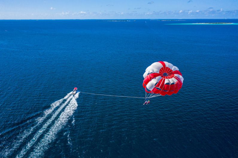 Maldives Ocean - a person is parasailing over the ocean with a boat